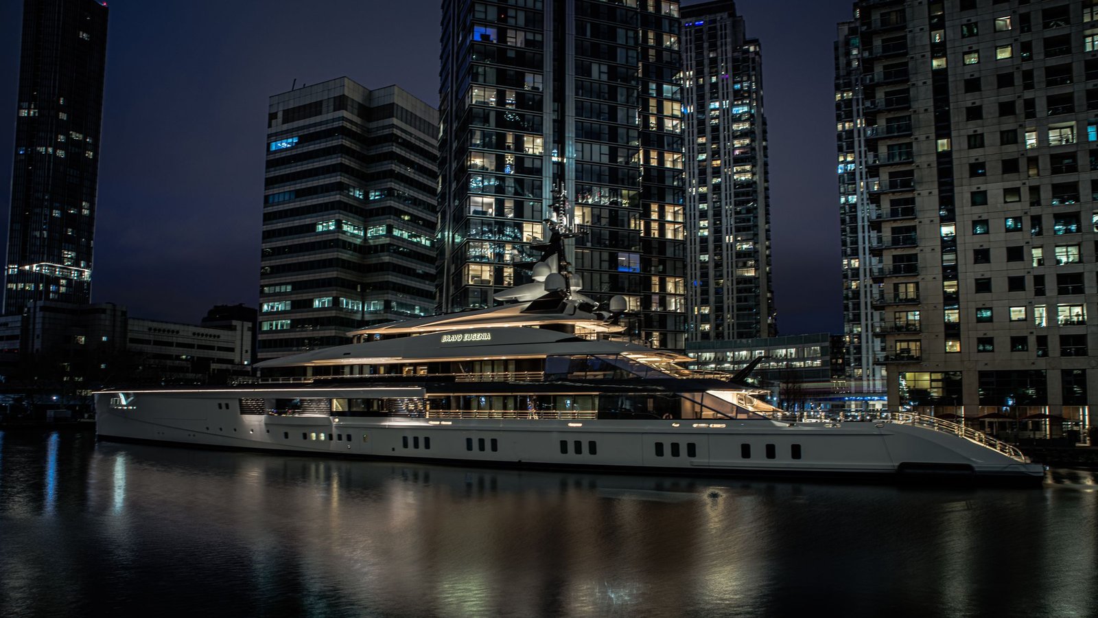 Beleuchtete Superyacht bei Nacht vor einer Skyline